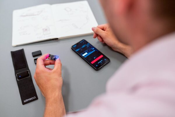 Engineer testing a wearable prototype using a smartphone interface at a desk.